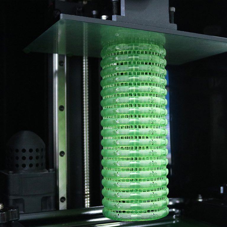 Several green resin bracelets in a batch being 3D - printed, showing a layered, ring - structured appearance during the printing process, with part of the 3D printer visible.