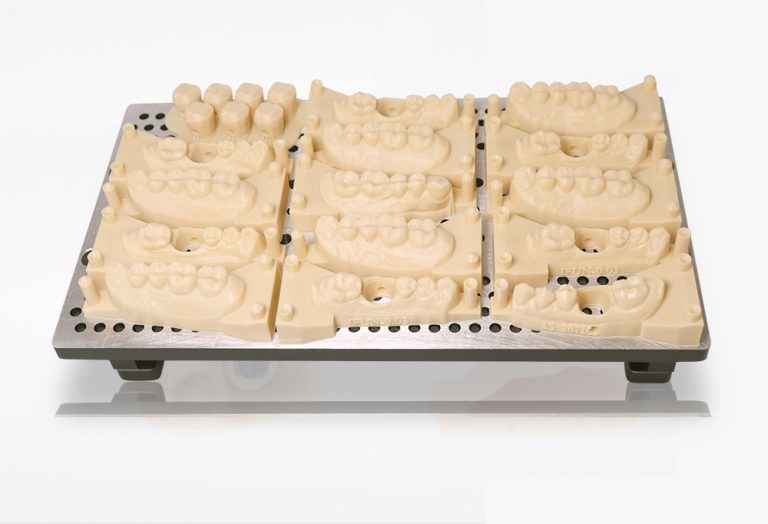 Multiple beige dental models arranged on a metal platform with holes, for dental 3D printing