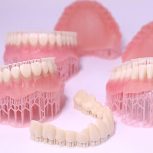 Pink denture bases printed with 1366 resin and white temporary crowns printed with 3164 resin, freshly printed with support structures still attached, ideal for dental study and prosthodontic procedures