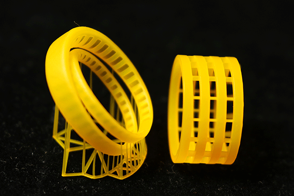 Two yellow ring prototypes made of castable resin, one with a multi - layer ring structure and support frame, the other with grid-like patterns
