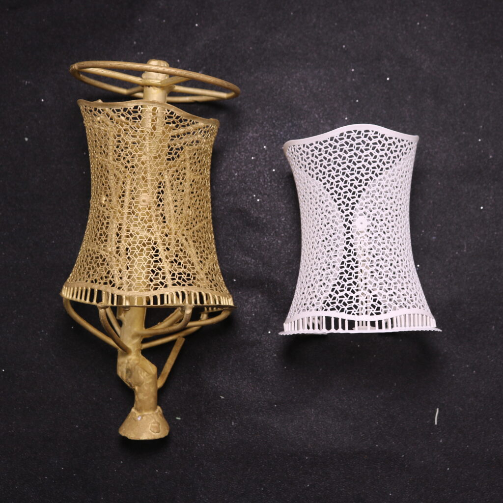 On a dark background, to the left is a golden - hued copper - cast bracelet with an intricate honeycomb - like lattice pattern. It has a top part with circular rings and a unique base structure resembling legs. To the right is a white 3D - printed bracelet made of white wax resin, also featuring a delicate honeycomb - style lattice design, with a smooth and slender appearance.
