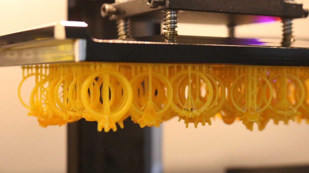 a newly printed ring hanging from the upside-down build plate of a resin 3D printer