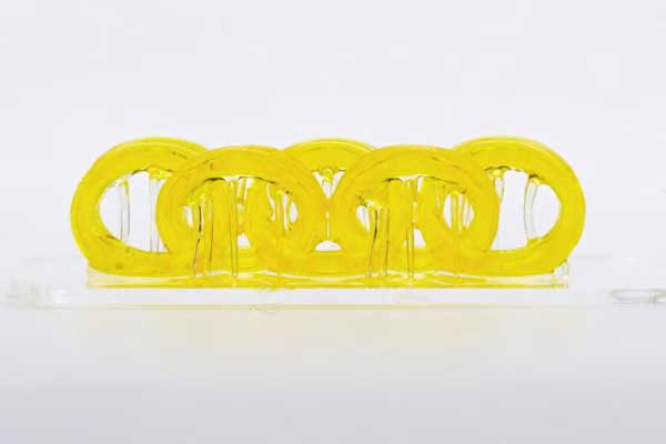 3D - printed structure created with a novel light - driven resin system. The yellow, interconnected ring - like form showcases flexibility, strength, and natural - inspired complexity, highlighting an innovative approach in additive manufacturing that mimics nature’s design principles.
