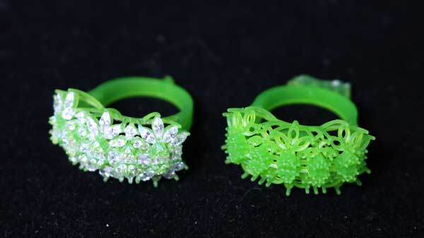 Two 3D - printed green resin rings featuring floral - shaped, diamond - adorned heads and open - work bands