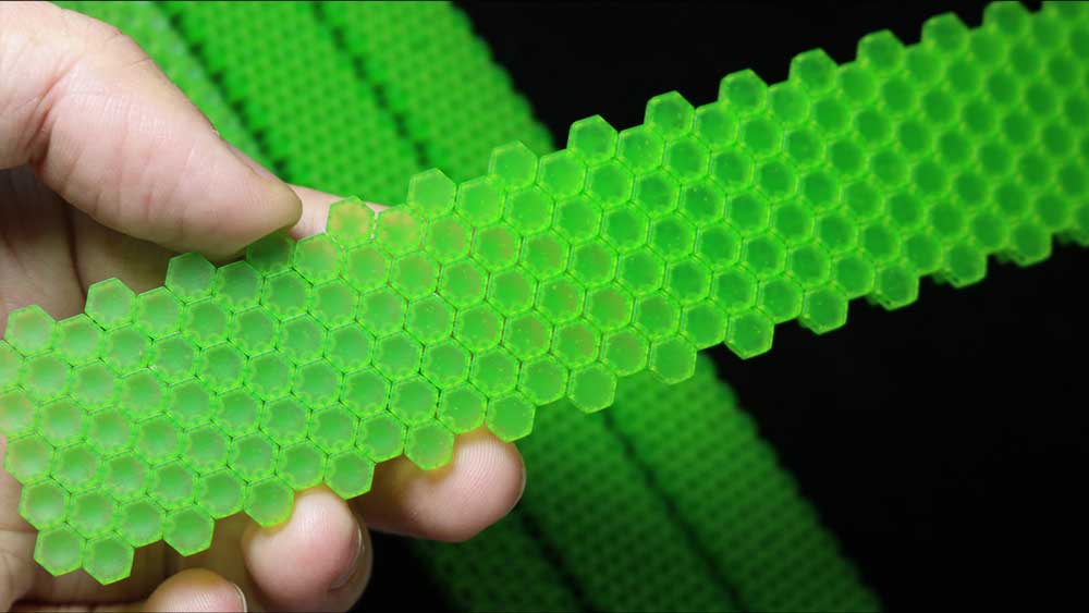 Hand holding a flexible 3D-printed green castable resin bracelet with a honeycomb structure, showcasing thin surfaces and clear tiny gaps