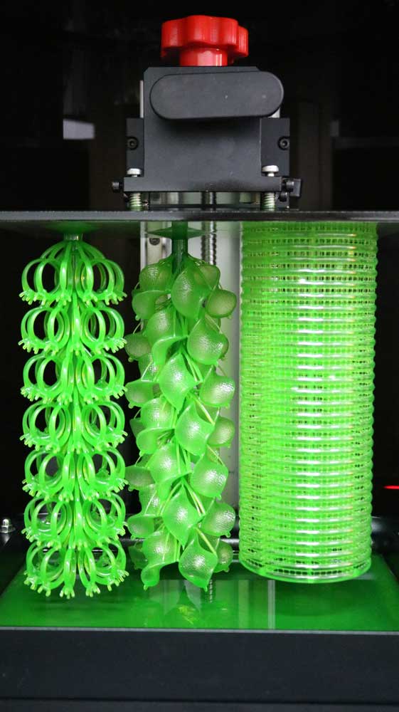 High-speed resin 3D printer build plate with freshly printed ring tree, earring tree, and bangle tree models.