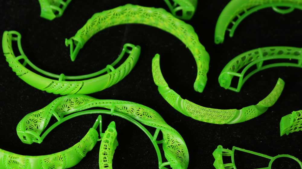 Multiple 3D - printed green castable resin bracelets featuring split-style clasp interlocks and intricate hollow textures