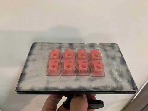 Eight pink 3D printed gingiva masks are shown on a metal build plate, highlighting the supports at the base of each model.