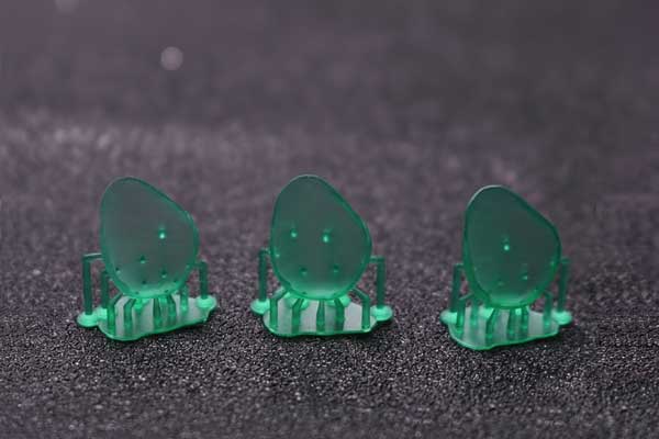 Three ultra-thin 3D printed dental veneer models in green resin, with supports still attached, showcasing the material's exceptional detail and dimensional stability for delicate casting.