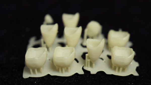 Multiple individual 3D printed crowns in VITA shades arranged on a 3D printing build platform.
