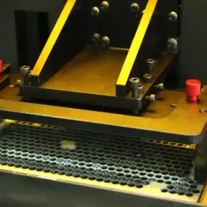 A close-up shot of a resin 3D printer's build plate submerged in a liquid resin vat with a perforated metal filter, showing the precision engineering of the printing process.