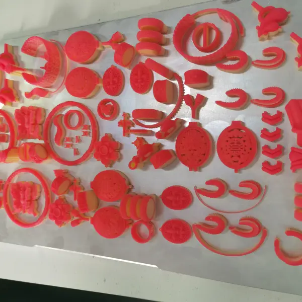 A metal build plate covered with numerous 3D printed red and white wax jewelry patterns.