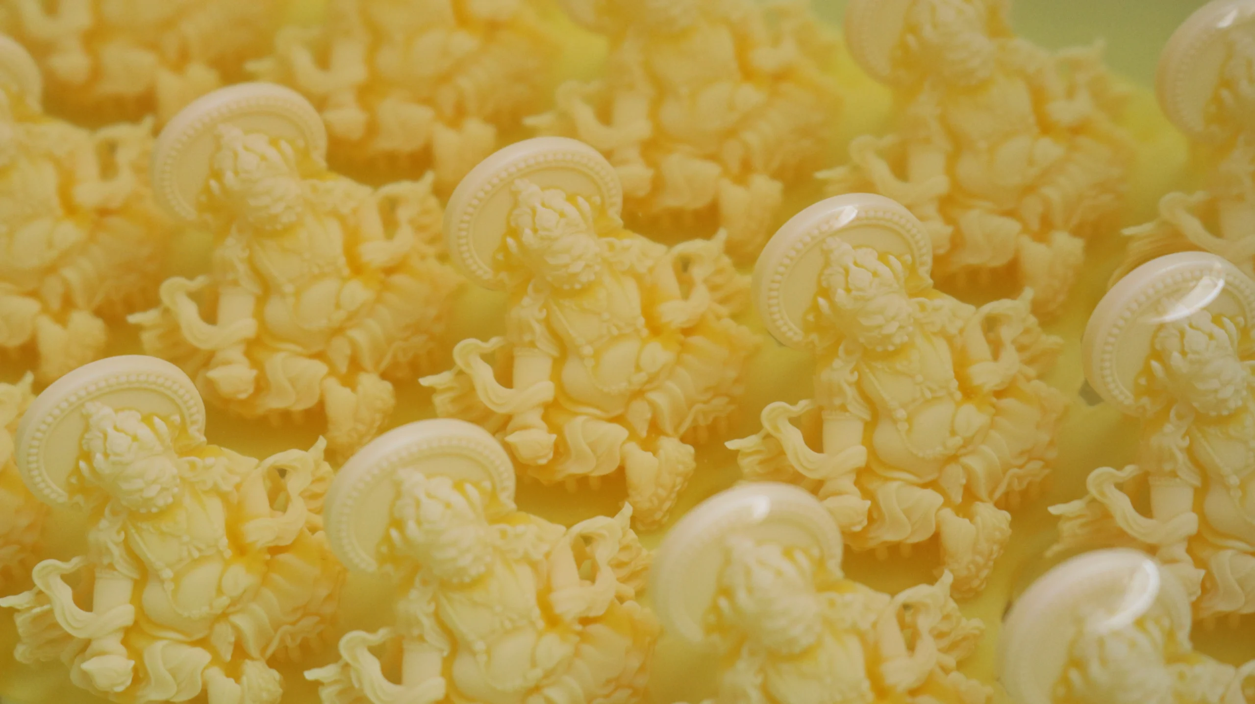 Close-up view of freshly 3D printed 800D wax Buddha pendants soaking in an alcohol cleaning bath
