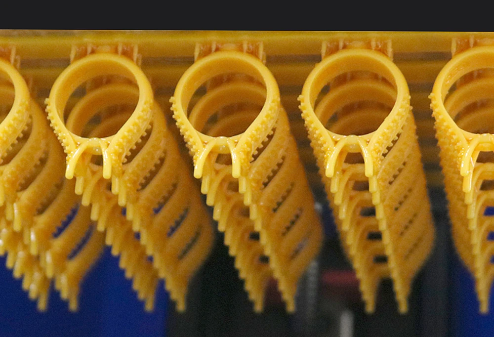 Macro close-up view of 3D printed solitaire ring mountings with prongs hanging on build plate