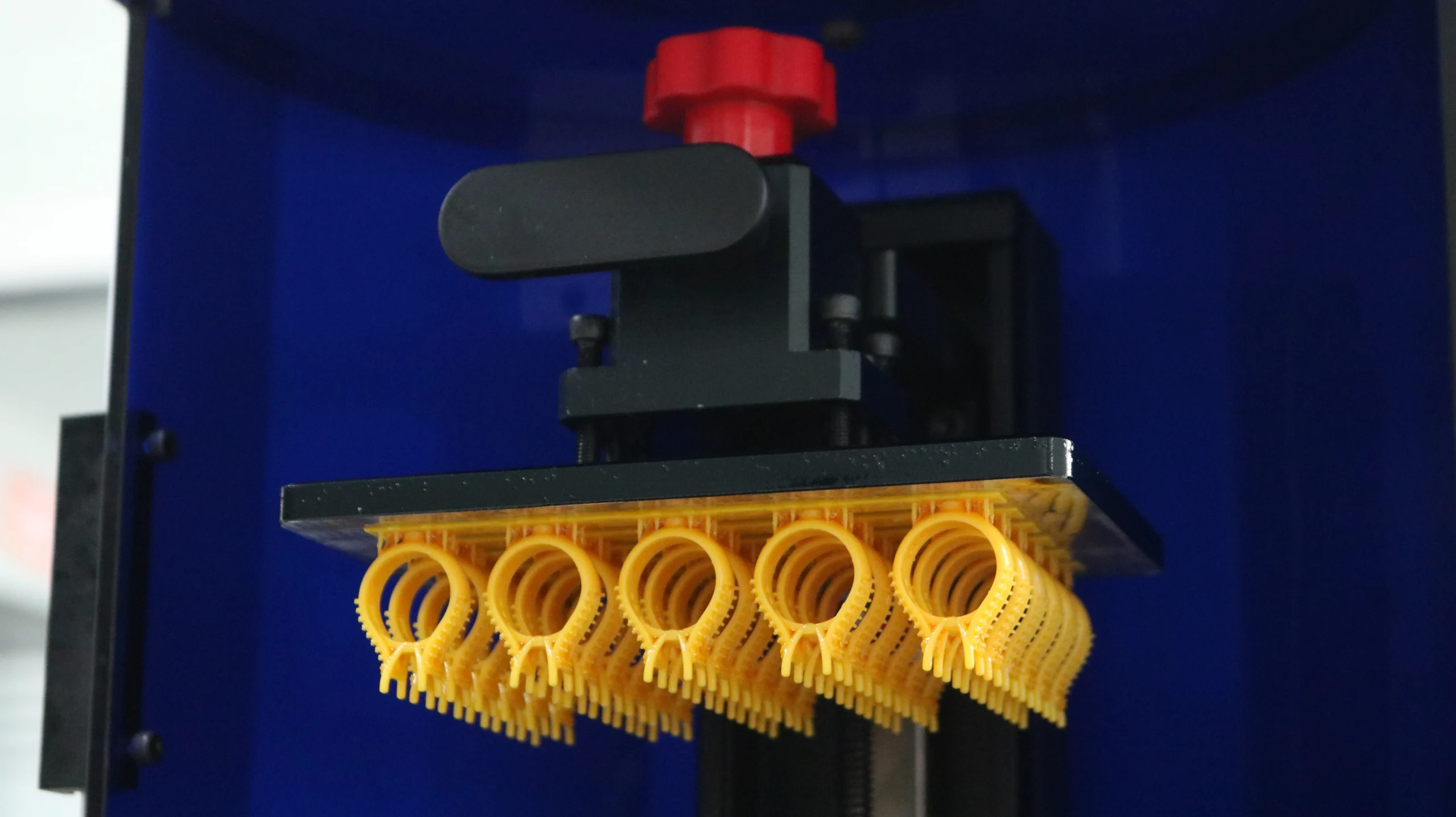 Wide front view of 3D printer chamber showing full batch of solitaire ring mountings on build plate