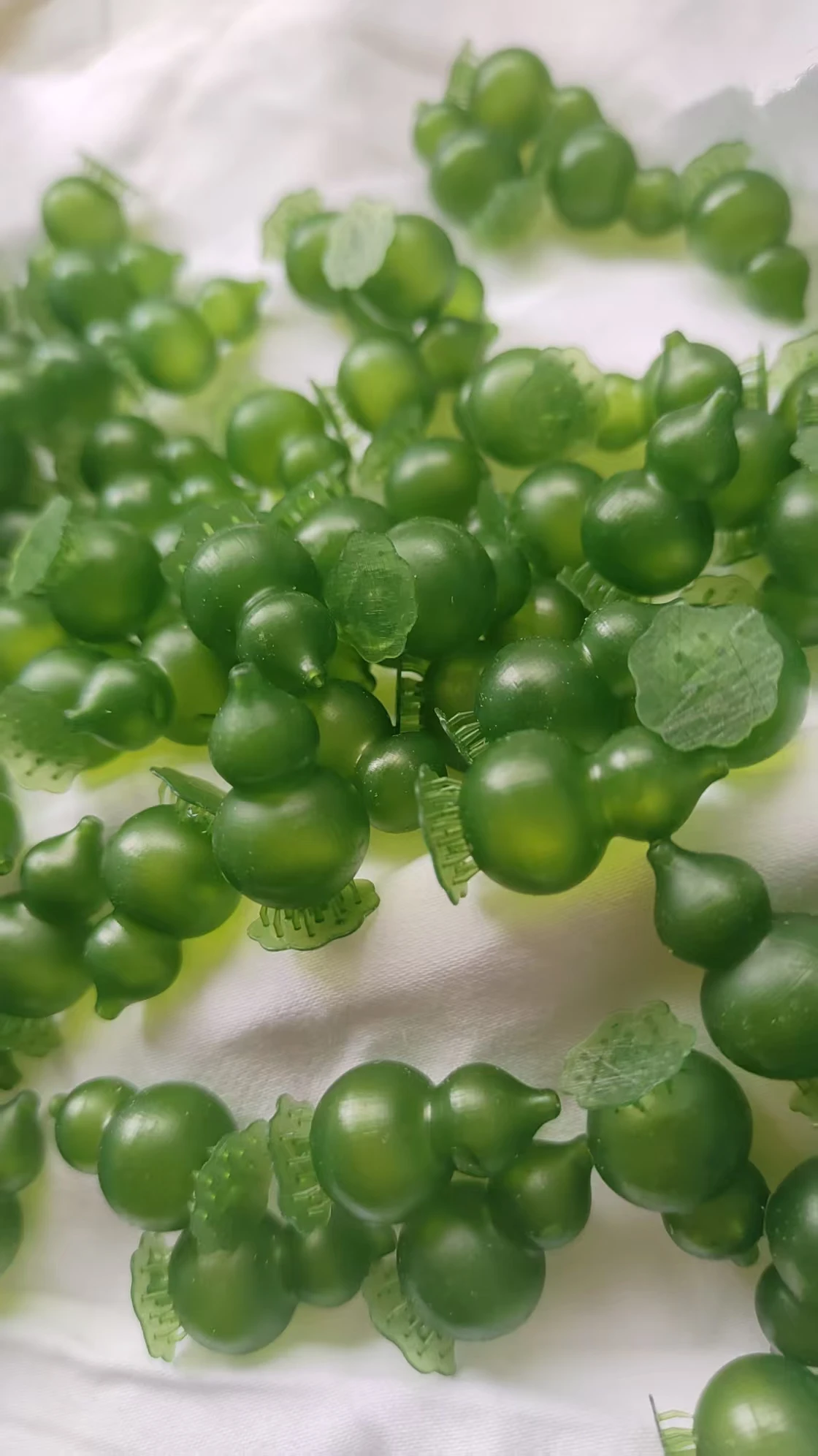 Batch-printed green gourd pendants 3D printed with IFUN 300H castable resin on a white fabric background.
