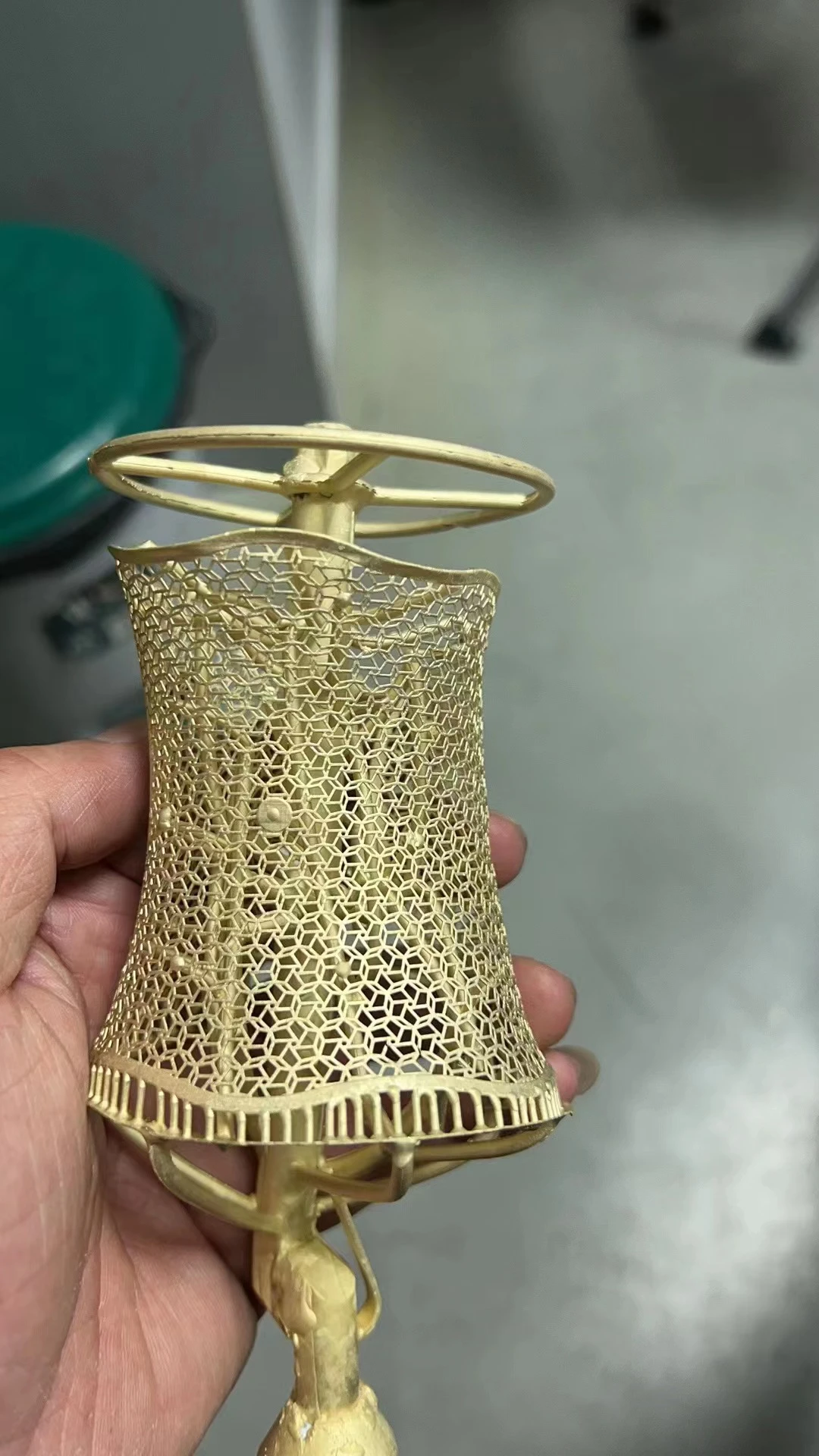 A freshly lost-wax cast brass openwork filigree bracelet with sprues still attached, held in a person's hand.