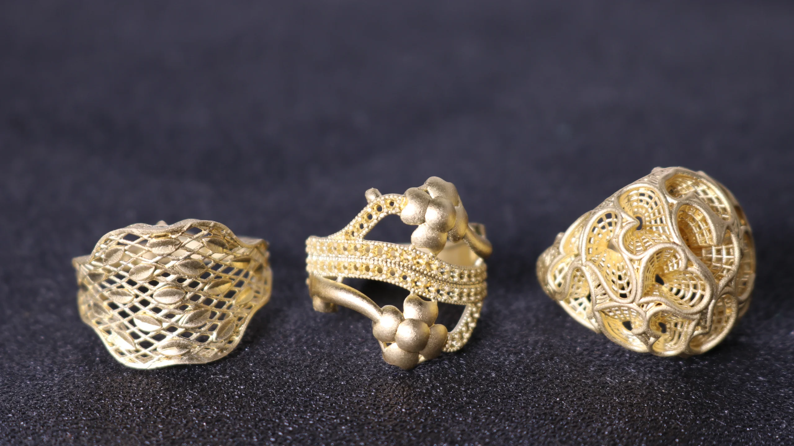 Front view of three raw gold cast rings featuring mesh lattice, pave setting, and filigree scrollwork