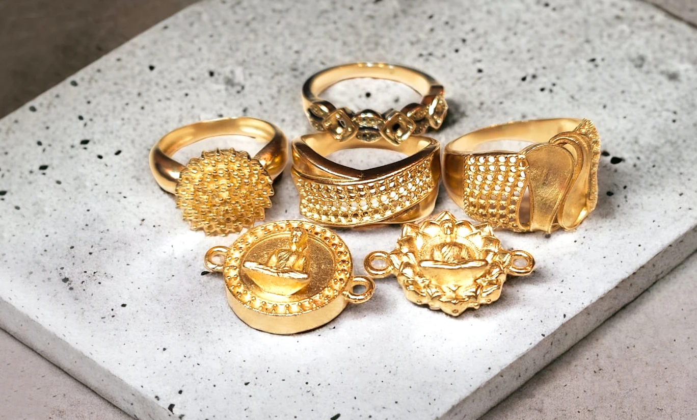 Perspective view of lost-wax gold cast jewelry including carved rings and Buddha pendants on stone slab