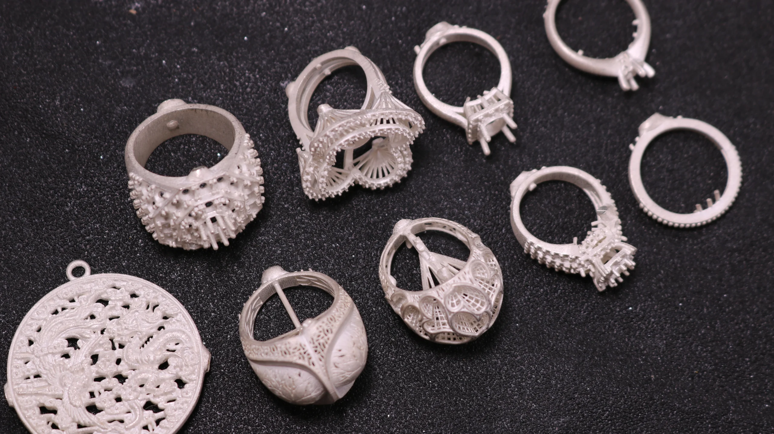 Top view flat lay of raw silver cast jewelry collection including pave rings and carved dragon medallion pendant